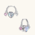 Silver chain hoop earrings with iridescent opal heart charms and pink zirconia accents on white background