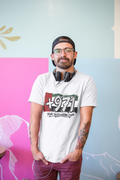 Man seated in a café wearing a white T-shirt with a +971 Your Destination Code graphic.