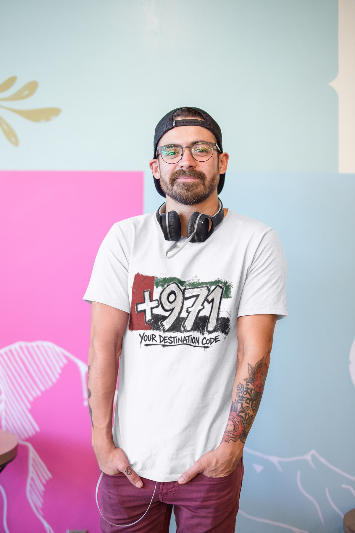Man seated in a café wearing a white T-shirt with a +971 Your Destination Code graphic.