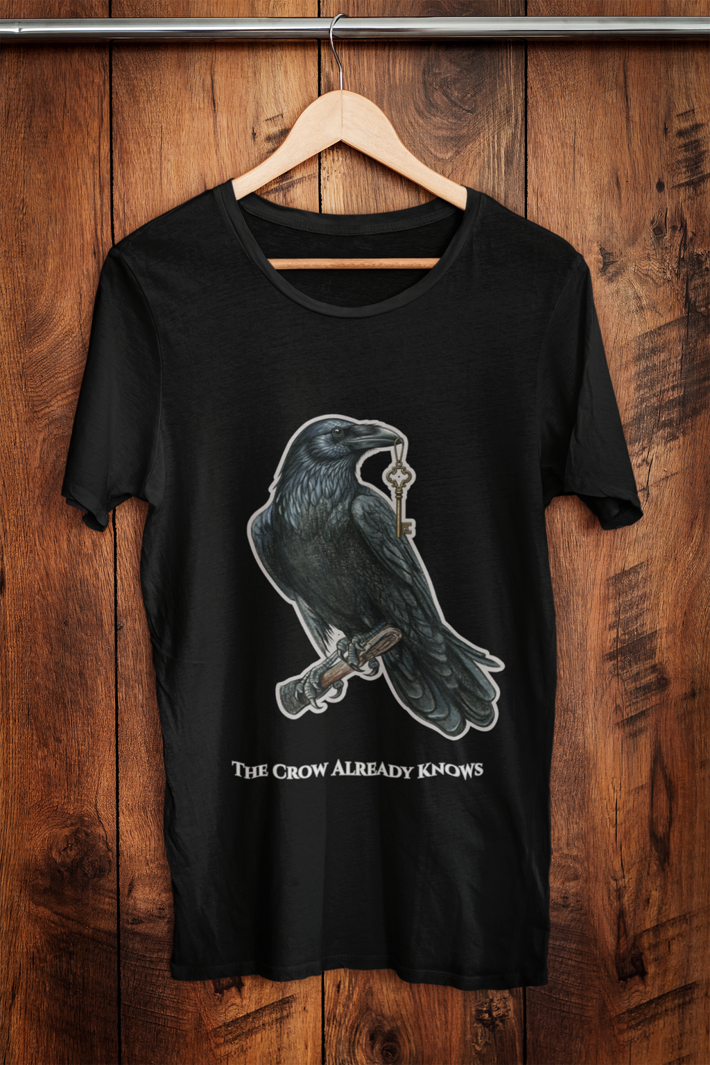 The Crow Already Knows graphic tee on hanger against wooden wall