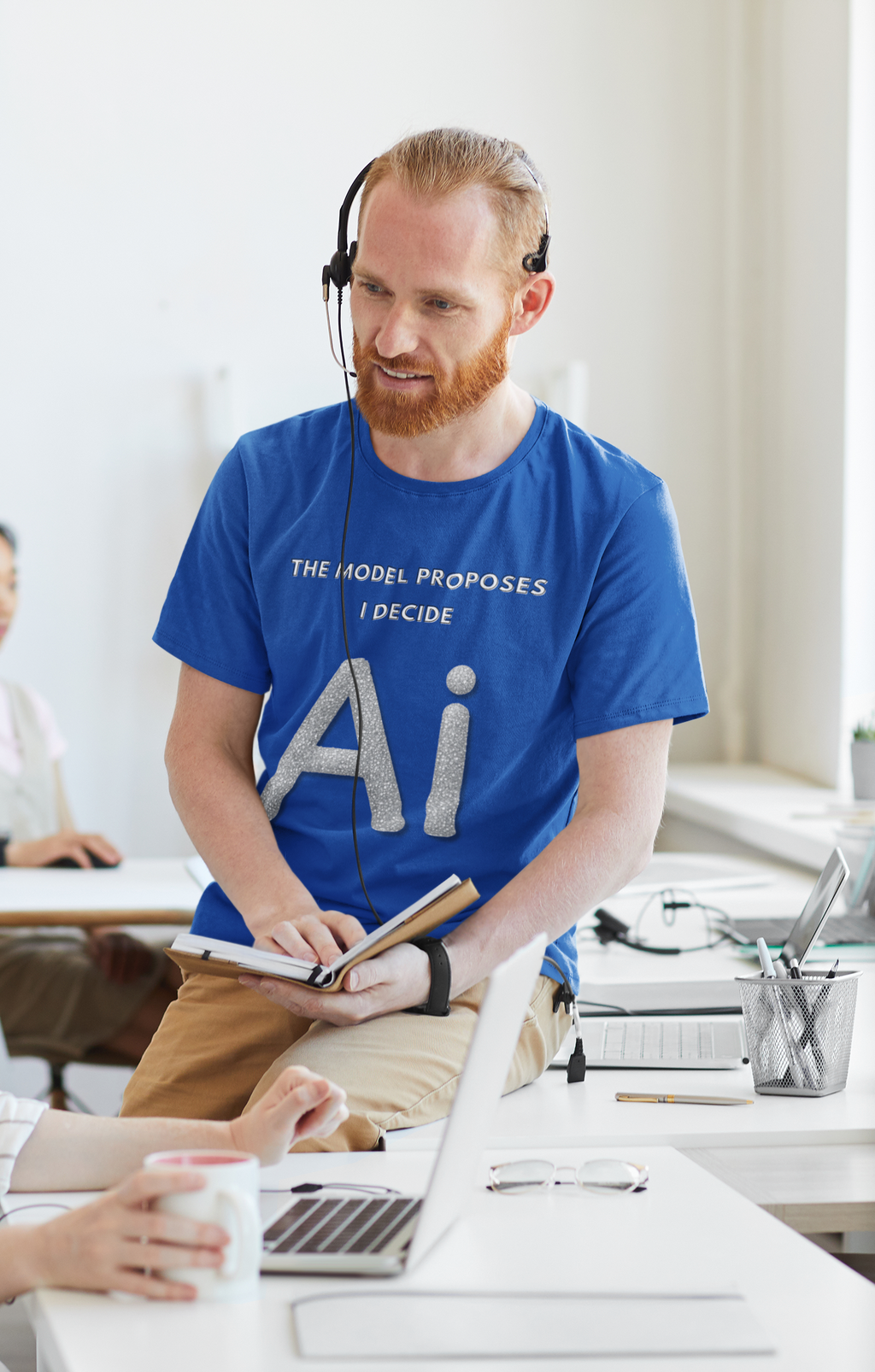 Man wearing a blue AI graphic T-shirt reading The model proposes, I decide in an office.