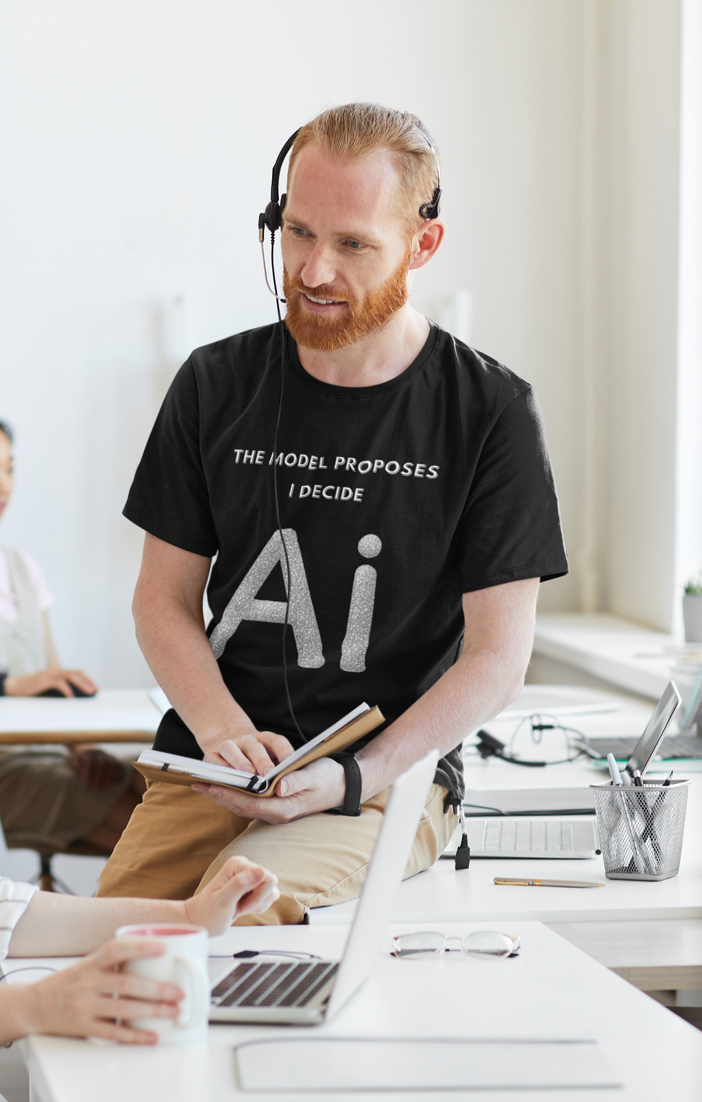 Man wearing a black AI graphic T-shirt reading The model proposes, I decide in an office.